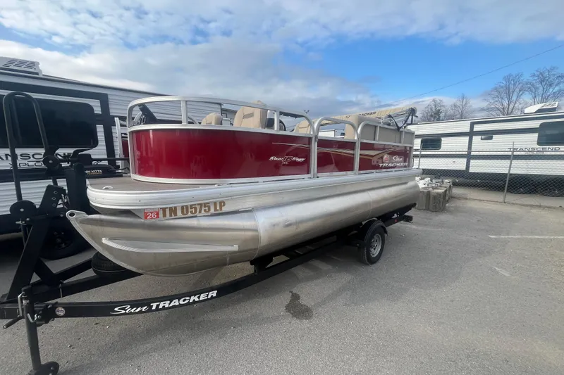 Slide: The Image of 2025 Sun Tracker Bass Buggy 16 XL Select pontoon boat on trailer, parked outdoors. - 2
