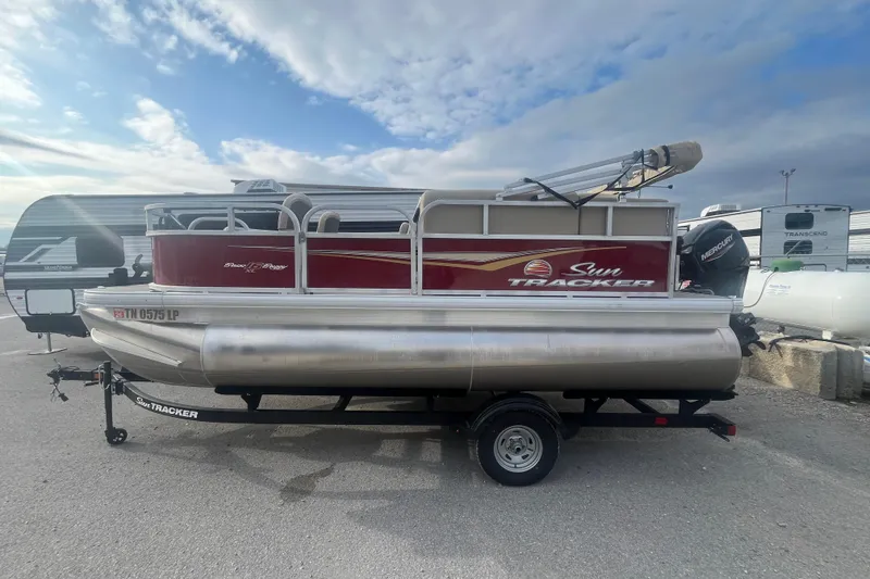 Slide: The Image of 2025 Sun Tracker Bass Buggy 16 XL Select pontoon boat on trailer, parked outdoors. - 4