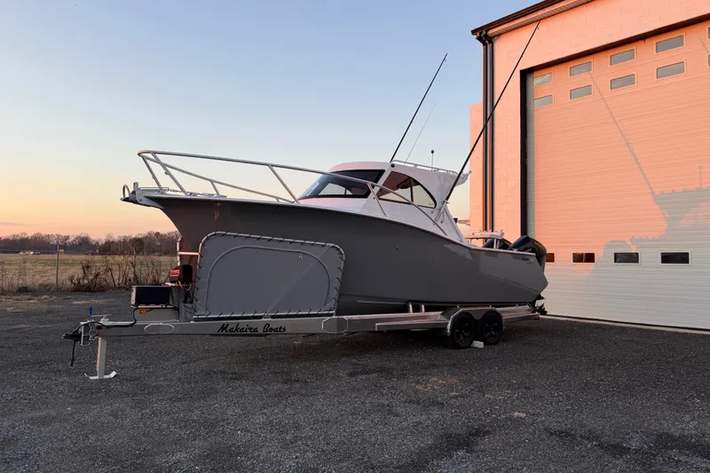 Slide: The Image of 2026 Makaira Gen3 26 Outboard boat on trailer near a building at sunset. - 49