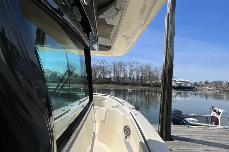 Slide: The Image of 2025 Scout 330 LXF boat docked by serene waterfront, clear blue sky. - 12