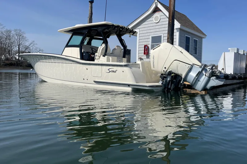 Slide: The Image of 2025 Scout 330 LXF boat docked on calm water near a small building. - 5