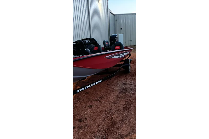 Slide: The Image of 2025 Tracker Pro Team 190 boat, red and black, parked on gravel near metal building. - 17