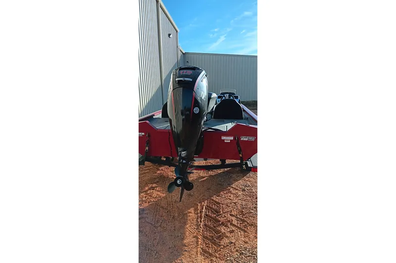 Slide: The Image of 2025 Tracker Pro Team 190 boat with outboard motor, parked on gravel near a building. - 6