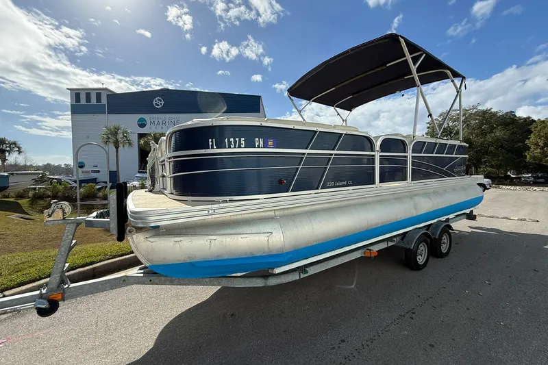 The Image of 2013 Silver Wave 220 Island CL pontoon boat on trailer, parked near marine center. - 0