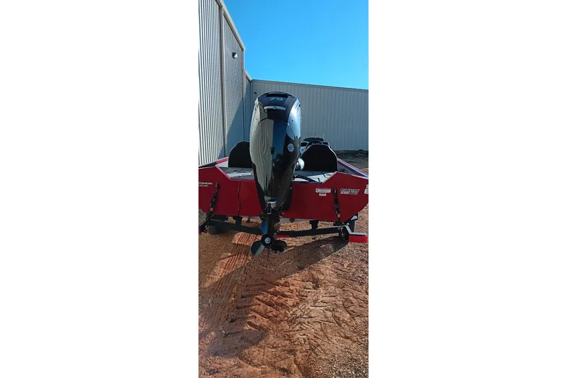 Slide: The Image of 2025 Tracker Pro Team 175 boat with outboard motor, parked on dirt near a building. - 19