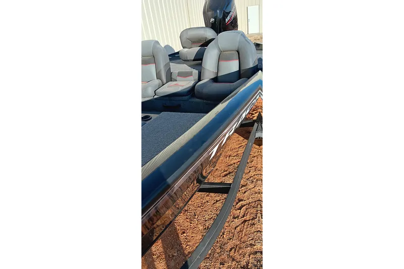 Slide: The Image of 2024 Tracker Pro Team 175 TXW boat interior with seating and motor, parked on sandy ground. - 3