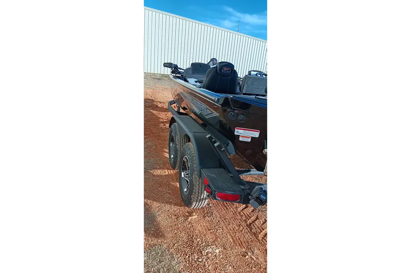 Slide: The Image of 2026 Ranger RT198P boat on trailer, parked on red dirt near a metal building. - 6