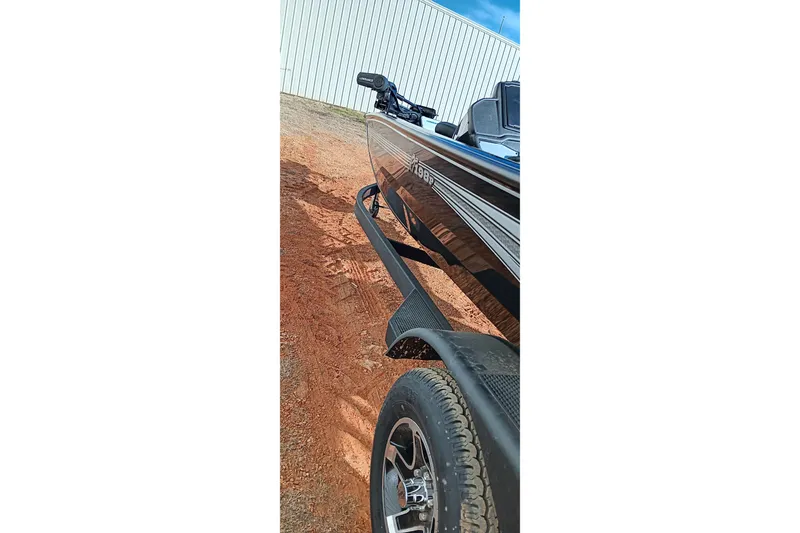 Slide: The Image of 2026 Ranger RT198P boat on trailer, parked on red dirt near a white building. - 7