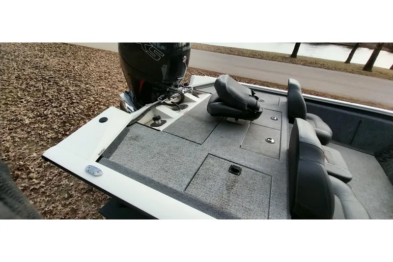 Slide: The Image of 2022 Tracker Pro Team 195 TXW boat interior with seating and motor, parked by a lakeside. - 5