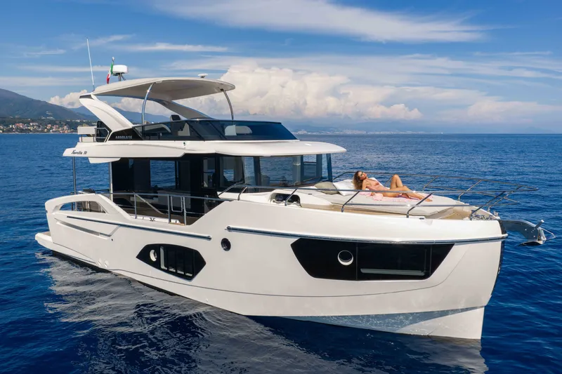 The Image of The 2027 Absolute 50 Navetta cruises on calm waters. A person relaxes on the foredeck. - 0