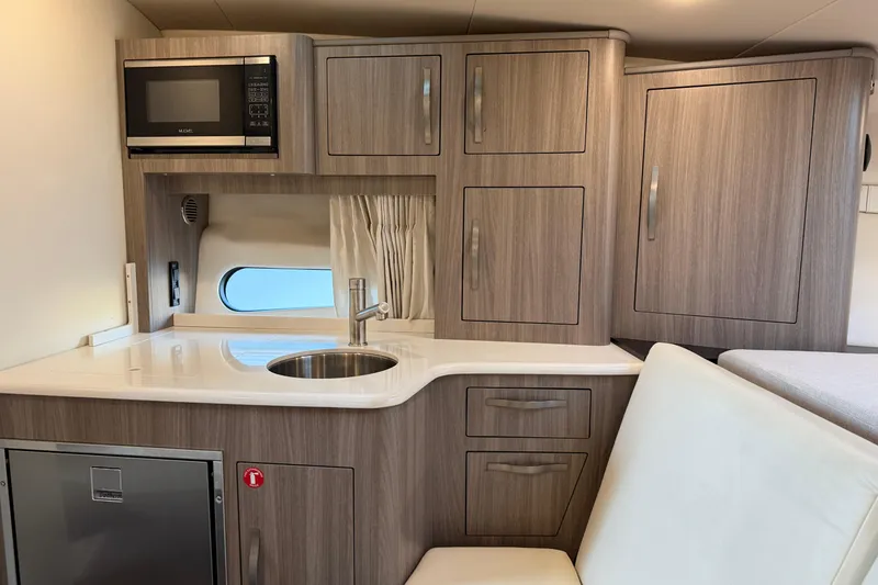 Slide: The Image of 2019 Regal 33 OBX boat interior kitchen with microwave, sink, and wooden cabinets. - 29