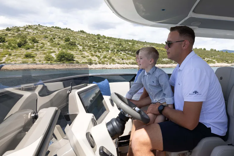 Slide: The Image of Father and son steering Absolute Navetta Co Ownership yacht, 2026 model, near scenic coastline. - 22