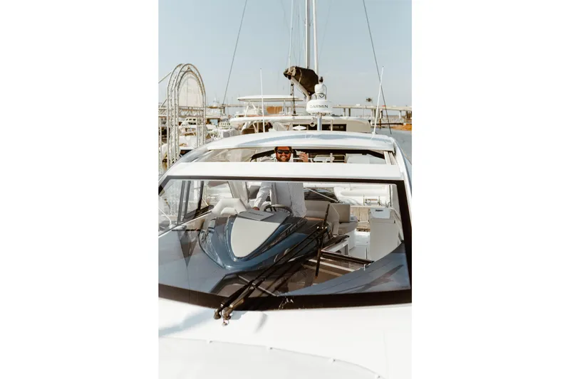 Slide: The Image of 2023 Beneteau Gran Turismo 41 yacht with a person at the helm, docked in a marina. - 2
