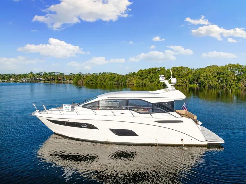 Slide: The Image of 2017 Sea Ray 460 Sundancer yacht on serene water with lush greenery background. - 13