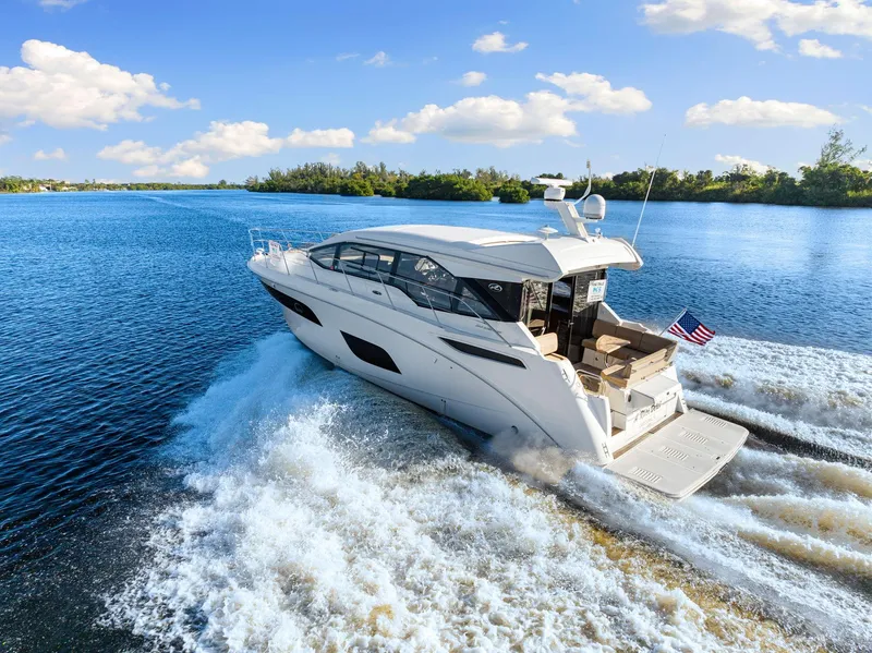 Slide: The Image of 2017 Sea Ray 460 Sundancer cruising on a sunny day, creating waves in a scenic waterway. - 4