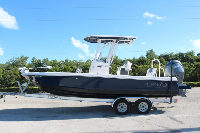 The Image of 2024 Robalo 226 Cayman boat on trailer, parked outdoors under clear blue sky. - 0