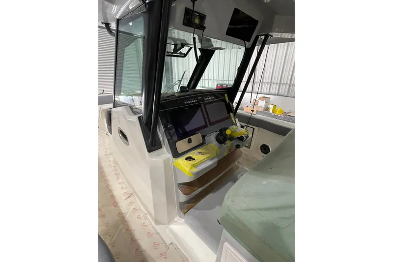 Slide: The Image of 2024 Boston Whaler 360 Outrage helm with modern navigation equipment in a boatyard setting. - 66