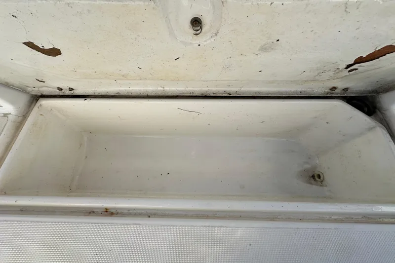 Slide: The Image of Open storage compartment on a 1999 Robalo 2420 Center Console boat, showing wear and rust. - 59