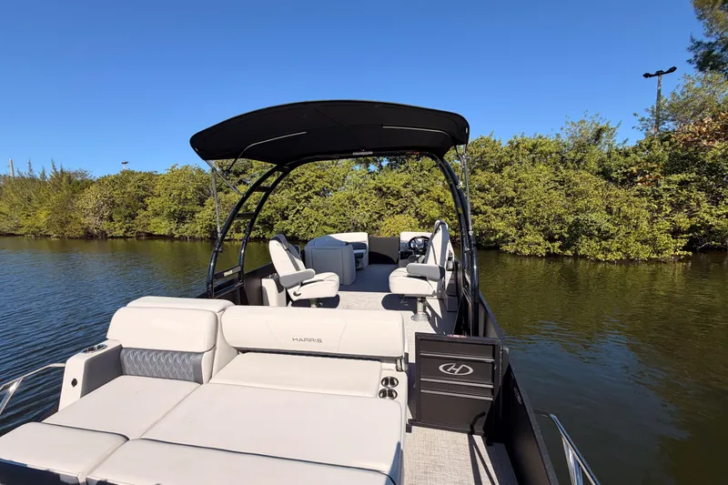 Slide: The Image of 2023 Harris Sunliner 230 Sport pontoon boat on a calm river, surrounded by lush greenery. - 21