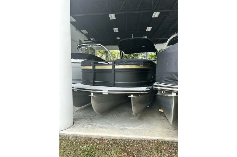 The Image of 2023 Harris Sunliner 250 Sport pontoon boat on trailer, covered and parked outdoors. - 1