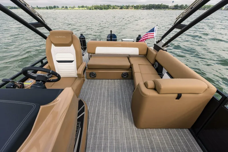 Slide: The Image of 2023 Harris Solstice 250 boat interior with tan seating and American flag on a lake. - 10