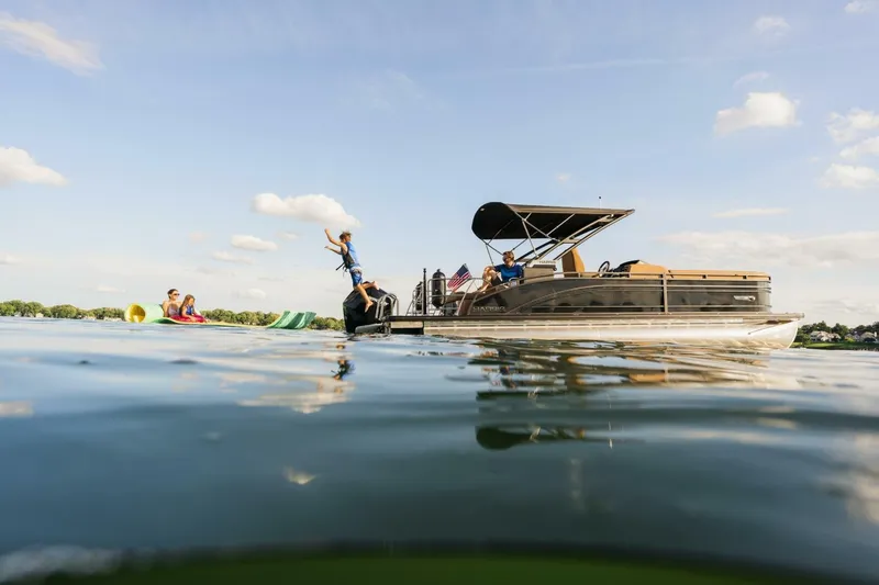 Slide: The Image of 2023 Harris Solstice 250 pontoon boat on a sunny lake with people enjoying water activities. - 4