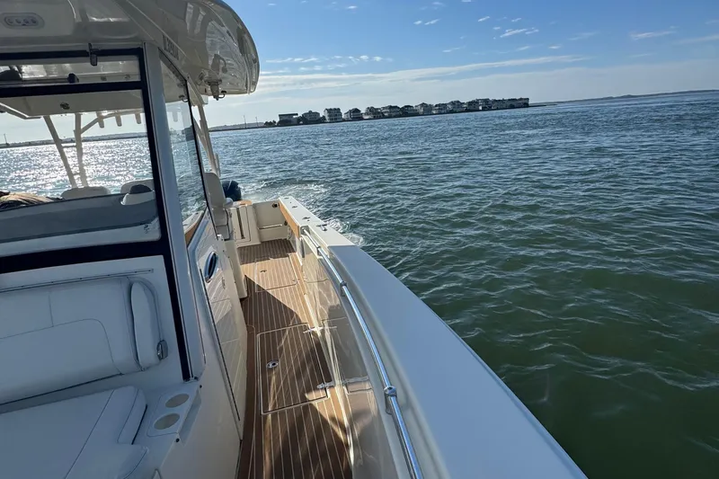 Slide: The Image of 2015 Cobia 344 Center Console boat cruising on a sunny day near coastal homes. - 13