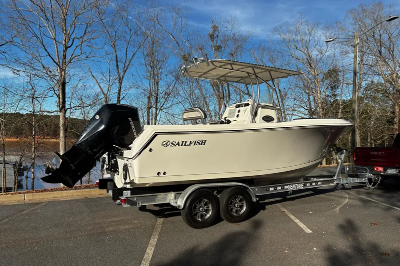 Slide: The Image of 2022 Sailfish 242 CC boat on trailer, parked near trees and lake. - 2