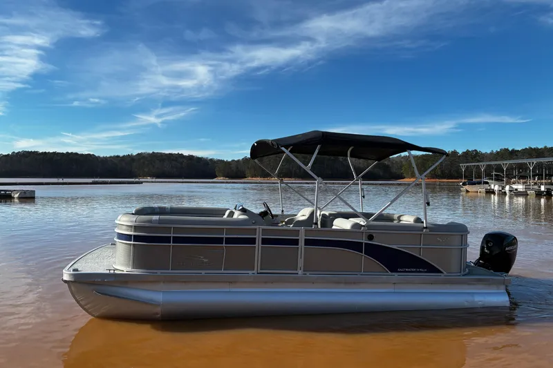 Slide: The Image of 2023 Bennington 22 SSR pontoon boat on a calm lake under a clear blue sky. - 2