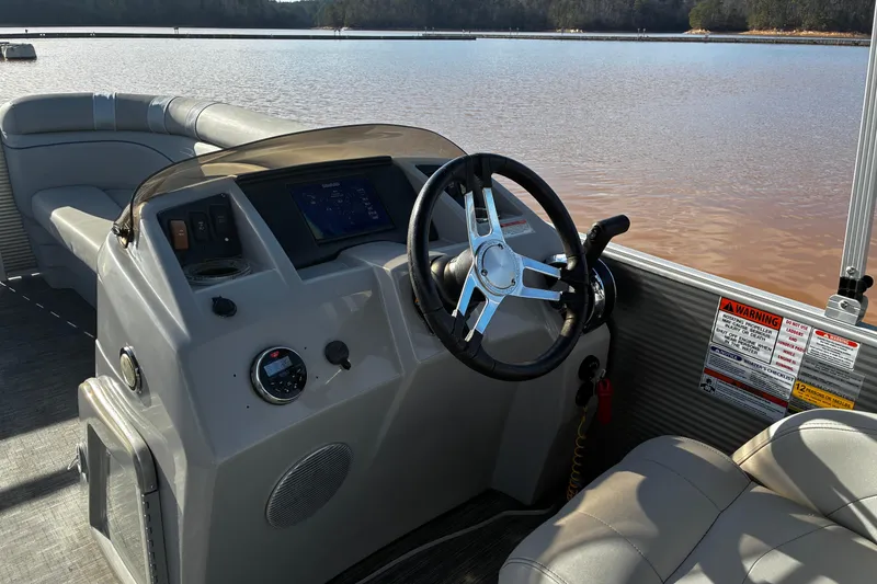 Slide: The Image of 2023 Bennington 22 SSR boat dashboard with steering wheel and controls on a calm lake. - 9