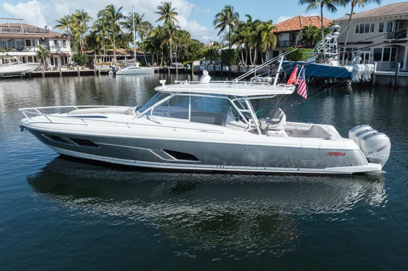 The Image of 2022 Intrepid 409 Valor boat on calm water, surrounded by palm trees and waterfront homes. - 0