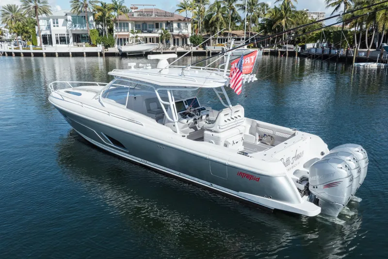 Slide: The Image of 2022 Intrepid 409 Valor boat on calm water, surrounded by palm trees and luxury homes. - 2