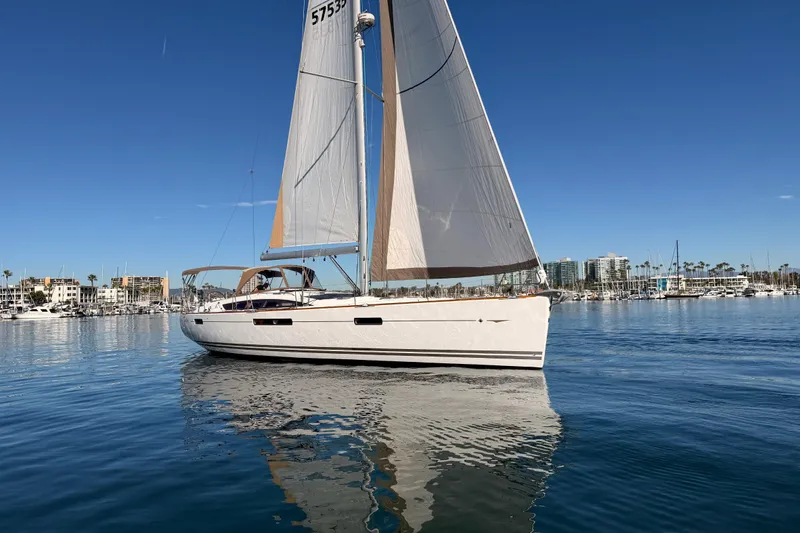 Slide: The Image of 2011 Jeanneau 53 sailboat on calm water with marina backdrop. - 2