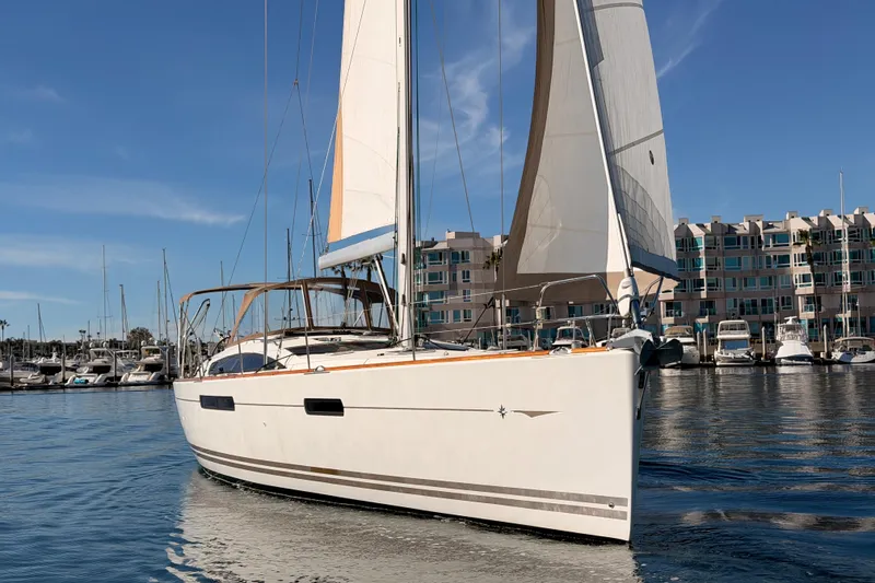 Slide: The Image of 2011 Jeanneau 53 sailboat docked in marina, clear sky, modern buildings in background. - 93