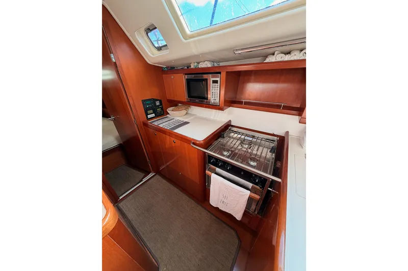 Slide: The Image of 2007 Beneteau 49 yacht kitchen with stove, microwave, and wooden cabinetry. - 50