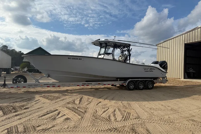 Slide: The Image of 2023 Cape Horn 34 XS boat on trailer, parked near a warehouse under a cloudy sky. - 11