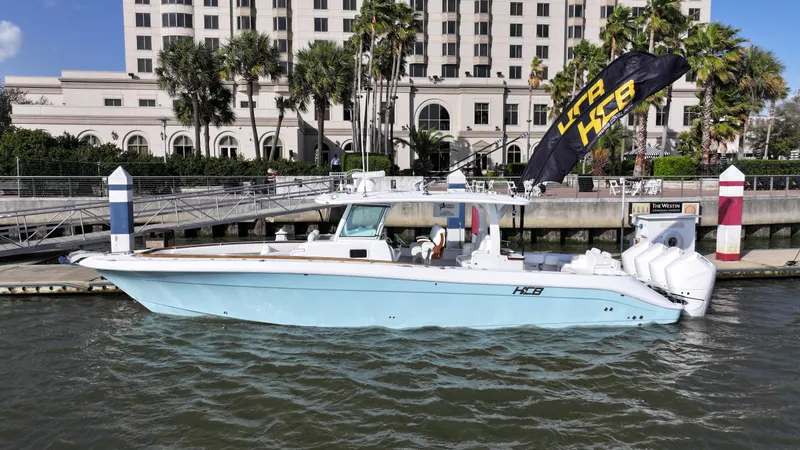 Slide: The Image of 2025 HCB Lujo boat docked by a waterfront building with palm trees. - 2