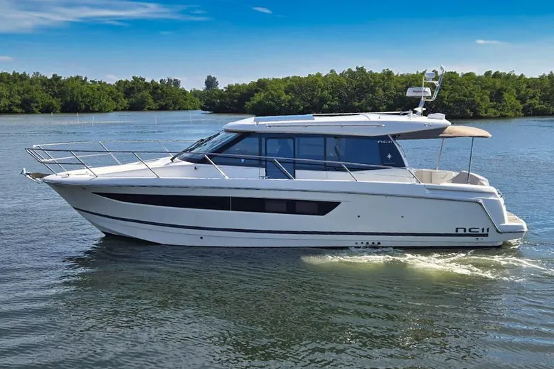 The Image of 2018 Jeanneau NC 11 boat cruising on a calm lake with lush greenery. - 0