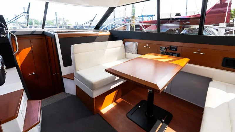 Slide: The Image of 2018 Jeanneau NC11 interior with dining area, white seating, and wooden table. - 12