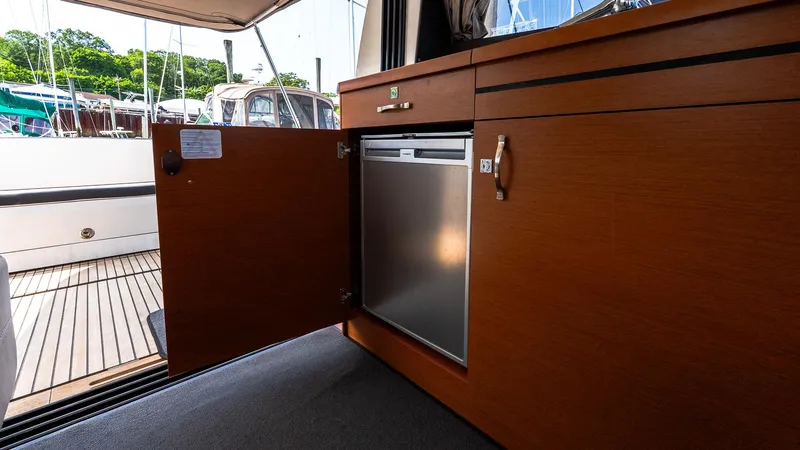Slide: The Image of 2018 Jeanneau NC11 interior with open cabinet revealing a compact refrigerator. - 21