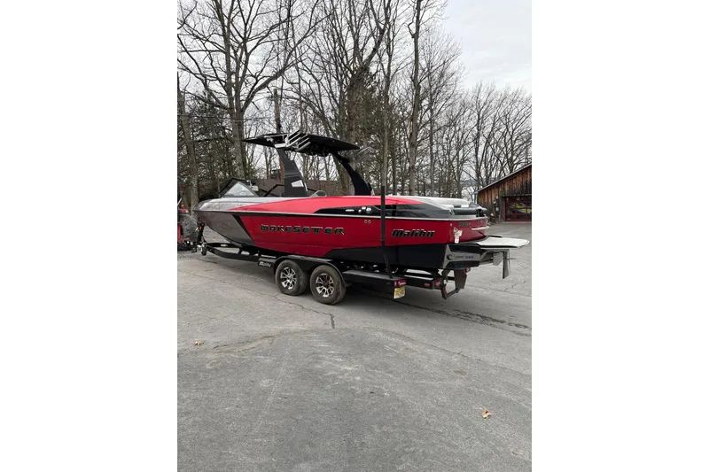 Slide: The Image of 2016 Malibu Wakesetter 25 LSV boat on trailer, parked outdoors, surrounded by trees. - 7