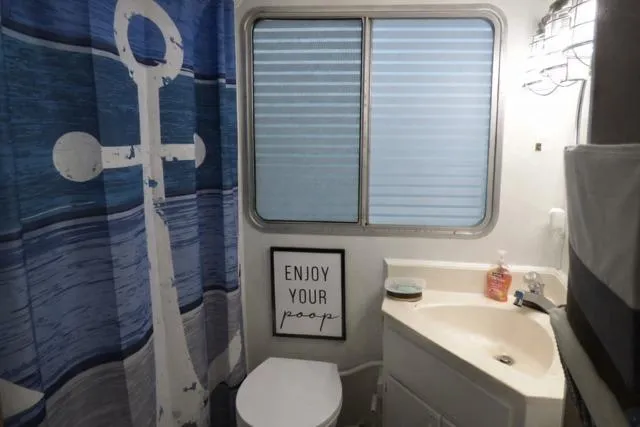 Slide: The Image of Bathroom in 1987 Sumerset 14x64 houseboat with anchor-themed shower curtain and humorous wall art. - 8