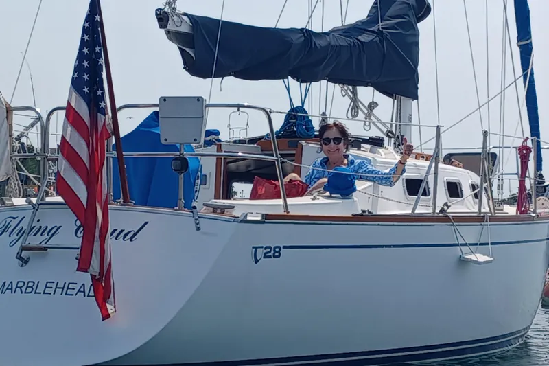 The Image of 1988 Tartan 28 sailboat with American flag, person smiling on deck, named "Flying Cloud." - 0