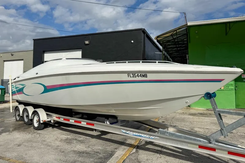 Slide: The Image of 1999 Baja 29 Outlaw speedboat on trailer, white with colorful stripes, parked outdoors. - 9