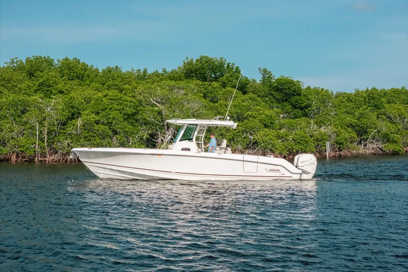 The Image of 2019 Boston Whaler 330 Outrage boat cruising near lush green shoreline. - 1