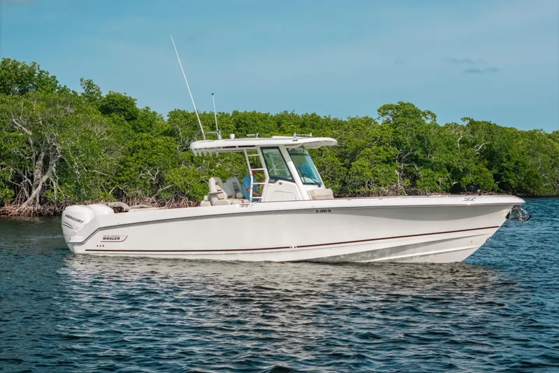 Slide: The Image of 2019 Boston Whaler 330 Outrage boat on calm water near lush green shoreline. - 26