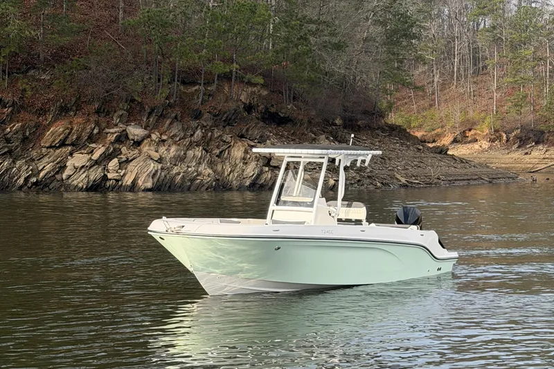 Slide: The Image of 2023 Bayliner Trophy T24CC boat on calm lake near rocky shoreline. - 2