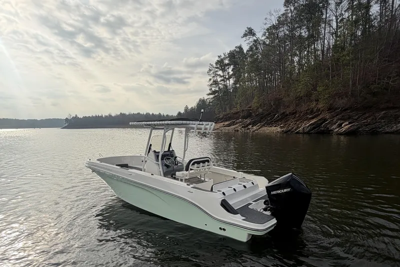 Slide: The Image of 2023 Bayliner Trophy T24CC boat on calm lake near forested shoreline. - 3