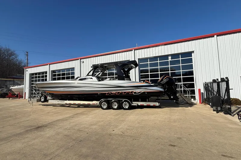 The Image of 2017 MTI 42V boat on trailer outside a garage under clear blue sky. - 1