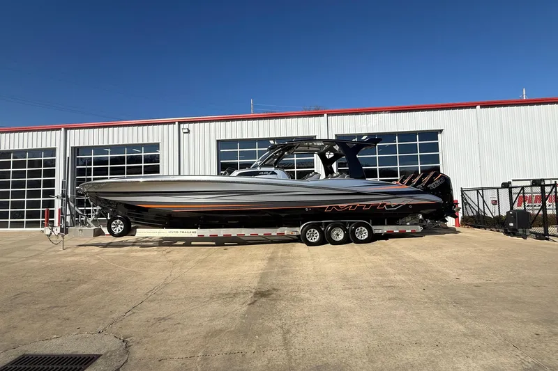 Slide: The Image of 2017 MTI 42V boat on trailer outside a garage, clear blue sky. - 2